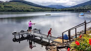 Man fishes from Briar Cottages jetty on Loch Earn with his son walking off the jetty.